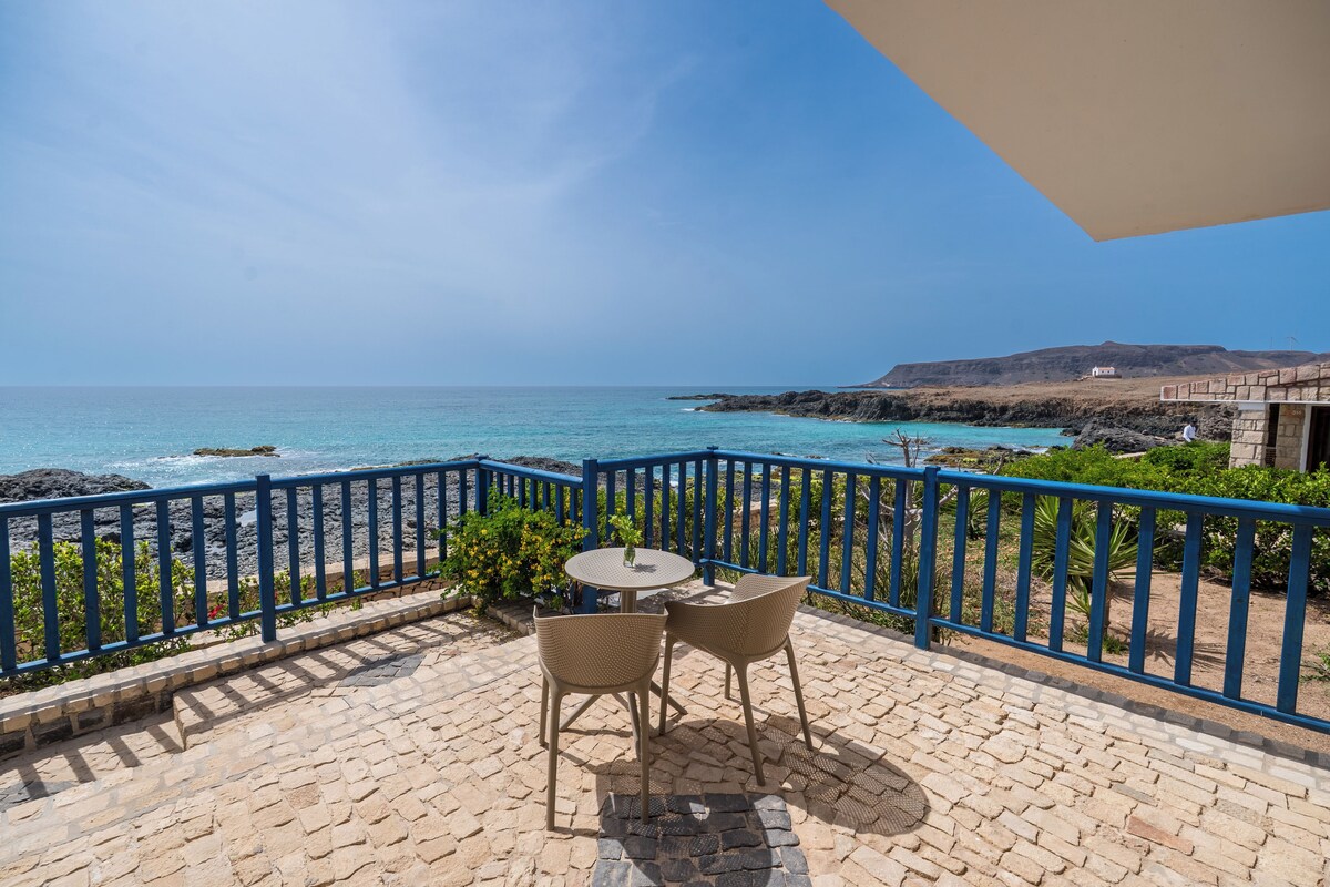 Een balkon met uitzicht op zee, met een tafel en twee stoelen.