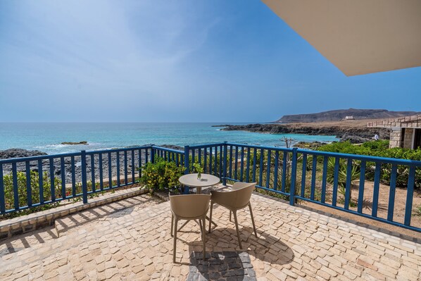 Un balcon avec vue sur la mer, une table et deux chaises.