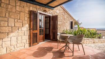 A stone building with a tiled patio, wooden shutters, and a view of the sea.