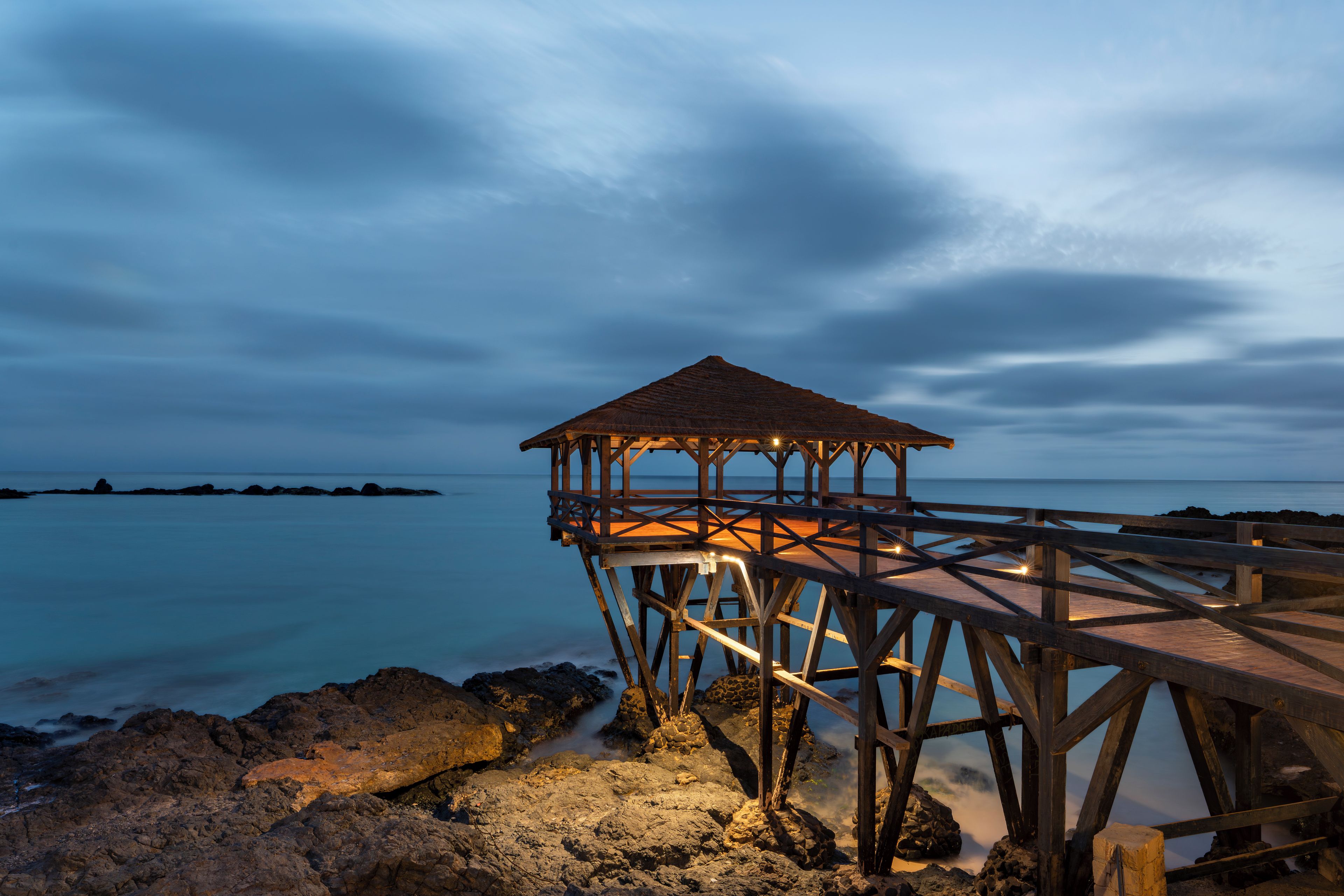 Un muelle de madera se adentra en aguas tranquilas, con una estructura de techo de paja al final.