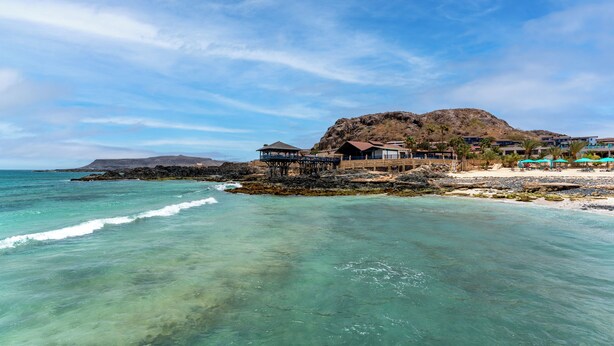 Un hôtel situé sur la côte, offrant une vue sur l’océan, avec une plage et un paysage montagneux en arrière-plan.