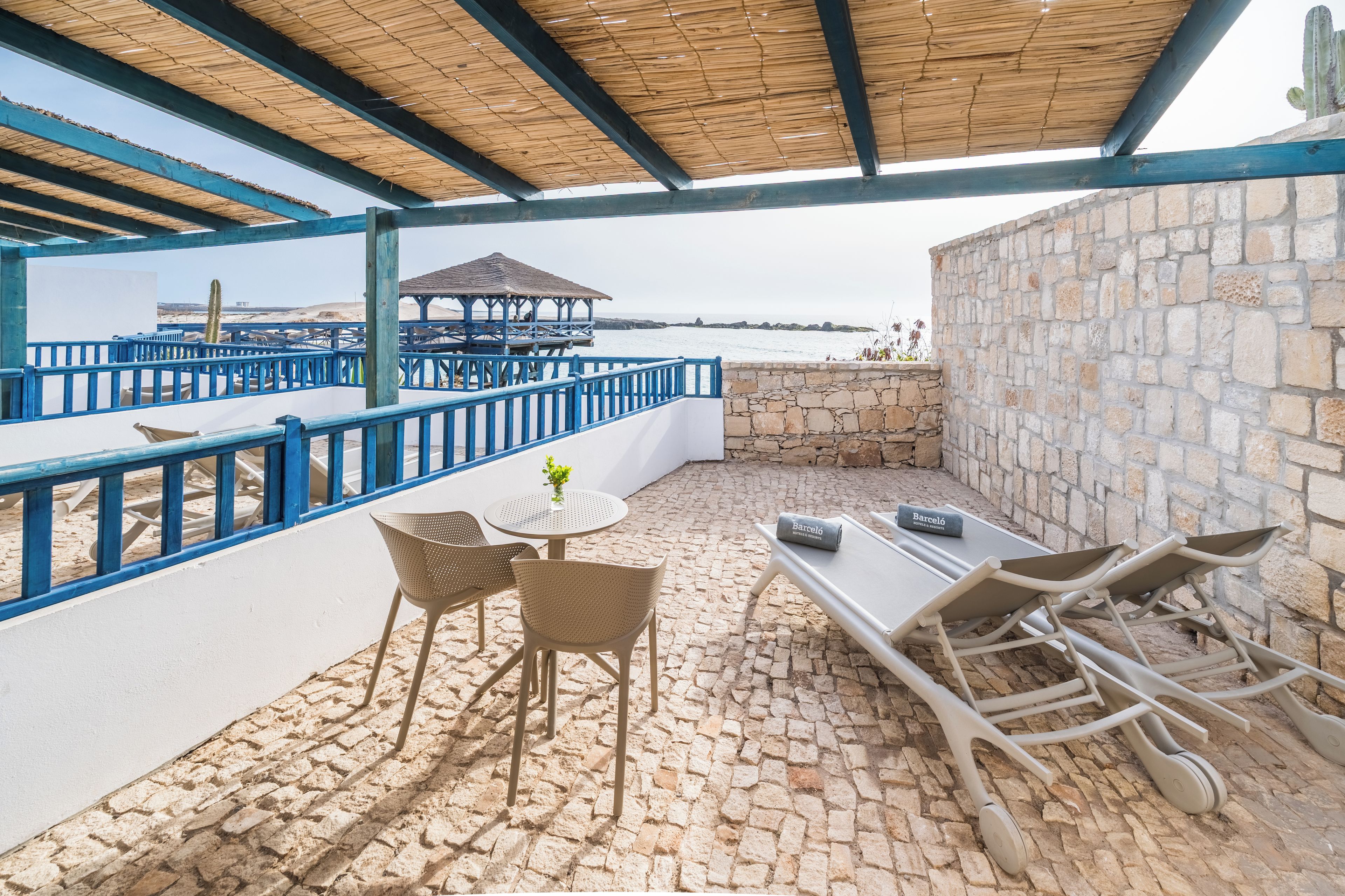 Un patio exterior con mesa y sillas, una mesita con un florero y vistas al mar.