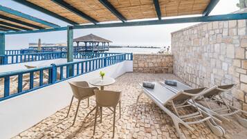 Un patio exterior con mesa y sillas, una mesita con un florero y vistas al mar.