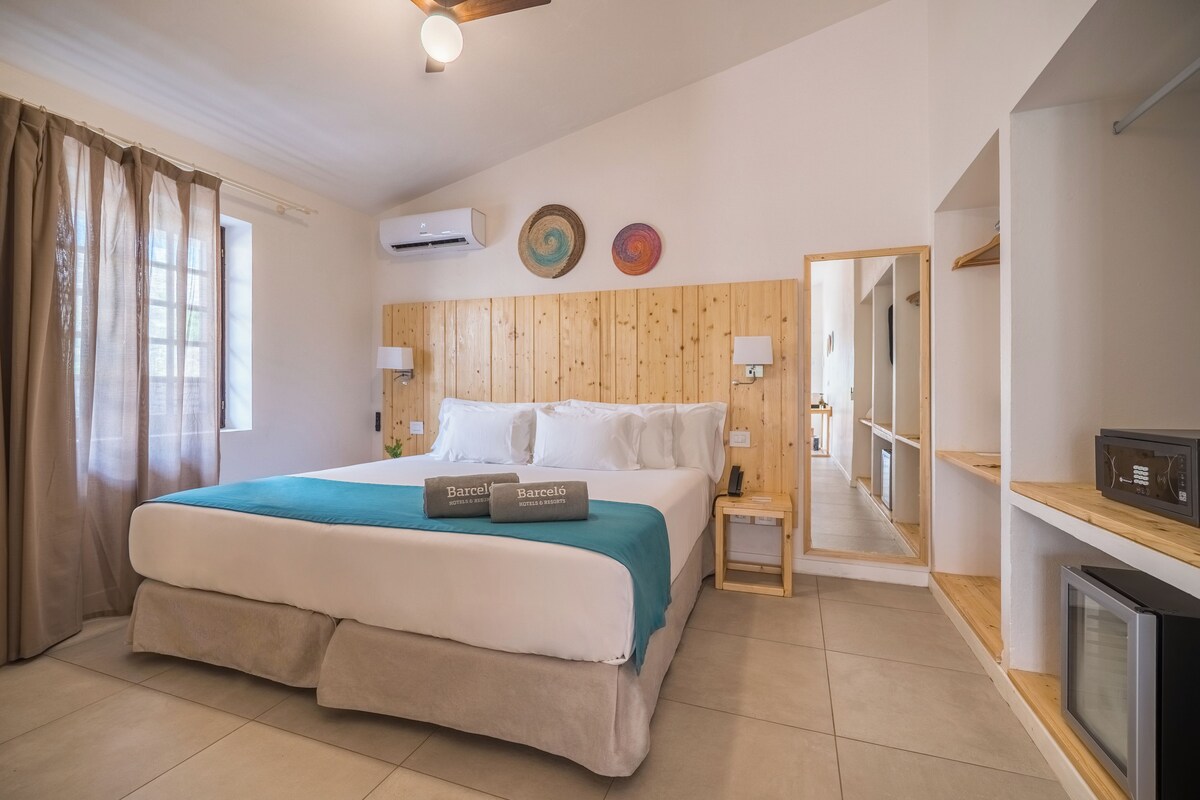 Een hotelkamer met een bed, nachtkastje, spiegel, televisie en raam met gordijnen.