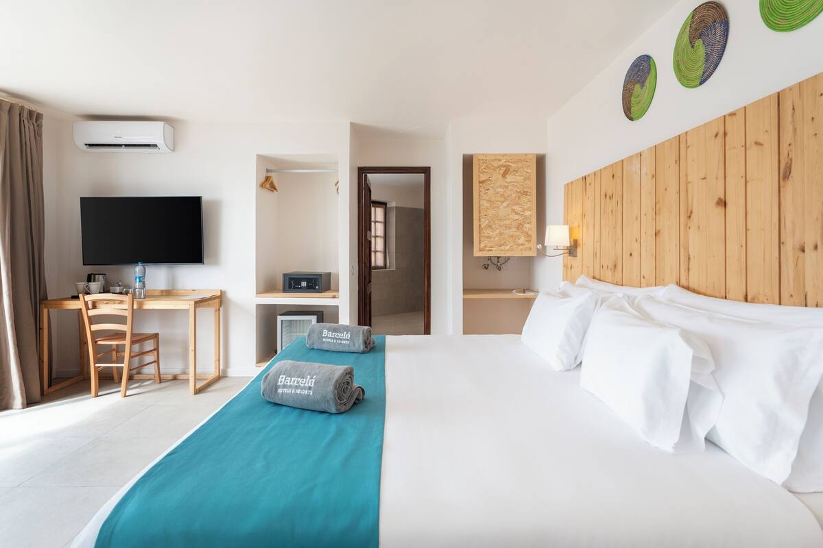 Habitación de hotel con una cama, un escritorio con una silla, un televisor y un cabecero de madera.