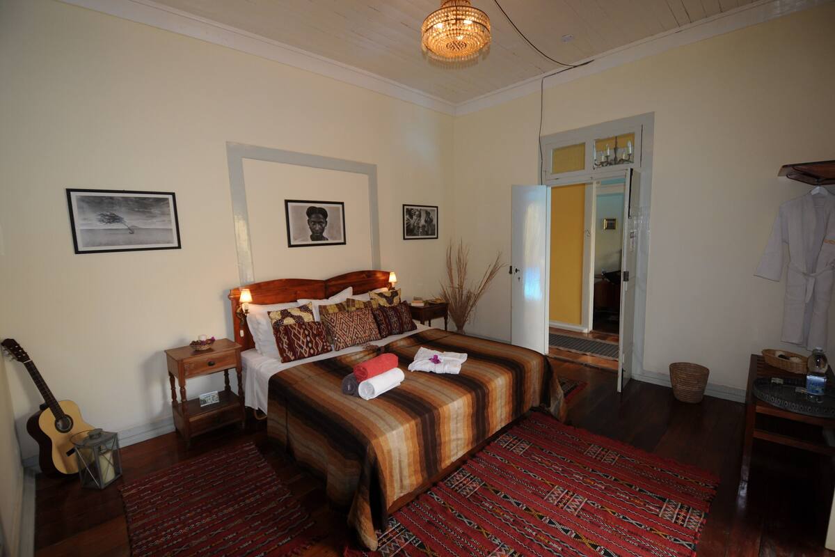 A bedroom with a wooden bed, a nightstand, a guitar, and a mirror.