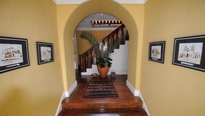 A hallway with wooden flooring, a large potted plant, and framed artwork on the walls. - The Colonial Guest House (São Filipe)