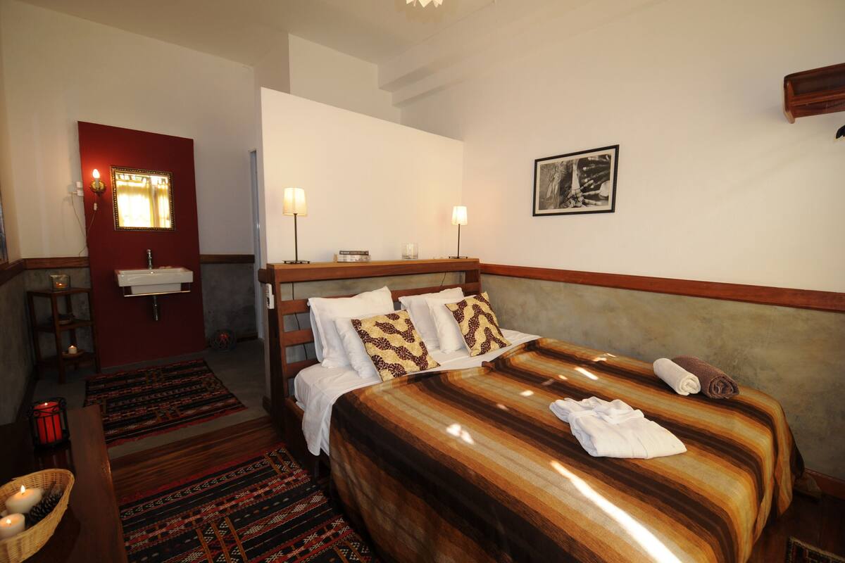 A hotel room with a bed, bedside lamps, a mirror, a small table with a candle, and a framed picture on the wall.