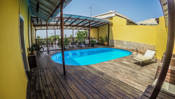 A wooden deck with a swimming pool, outdoor furniture, and potted plants. - The Colonial Guest House (São Filipe)