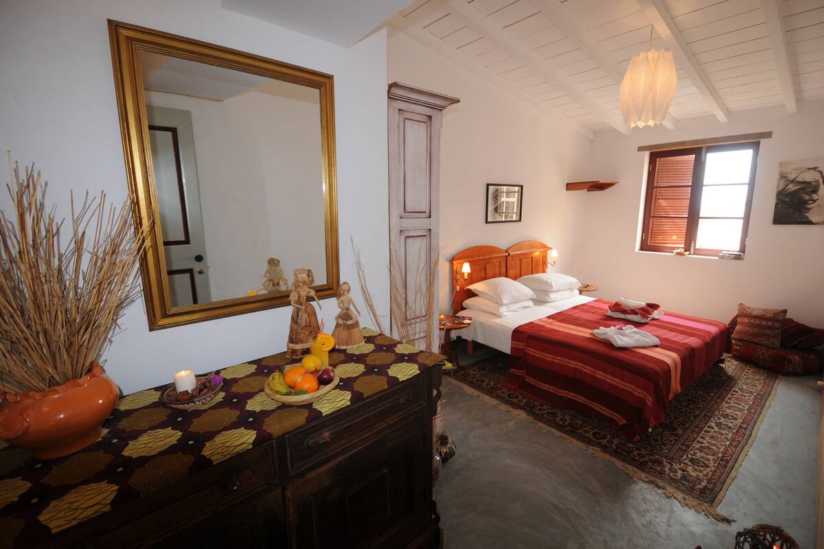 A bedroom with a large mirror, two beds, a dresser, and a window with shutters.