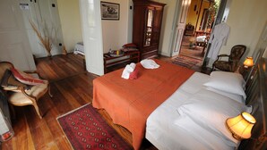 A hotel room with a large bed, a wooden wardrobe, a sitting area with a chair, and a small table with a vase and a tray. - The Colonial Guest House (São Filipe)