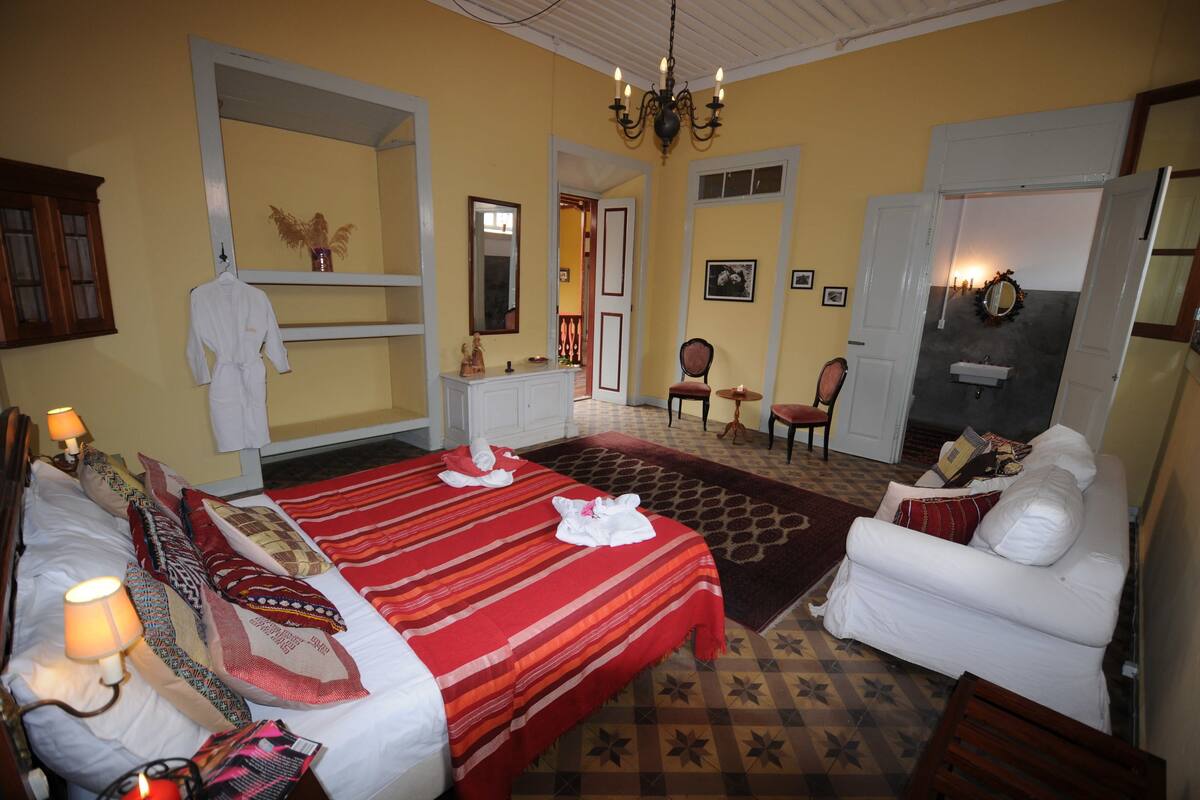A hotel room with two beds, a sitting area with a white sofa, a chandelier, and a mirror.