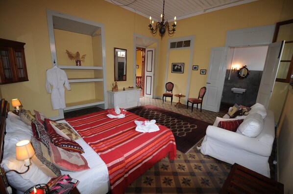 A hotel room with two beds, a sitting area with a white sofa, a chandelier, and a mirror. - The Colonial Guest House (São Filipe)