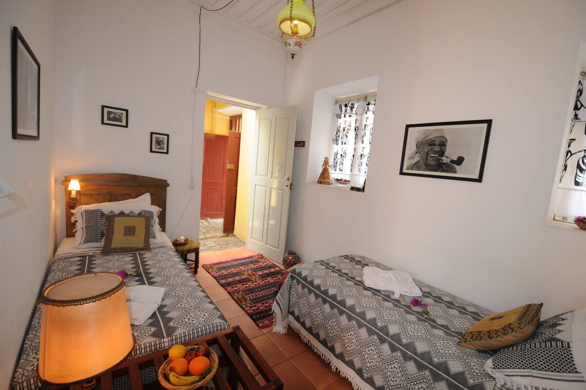 A room with a bed, a sofa, a lamp, a table with fruit, and a window with curtains.