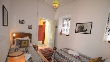 A room with a bed, a sofa, a lamp, a table with fruit, and a window with curtains.