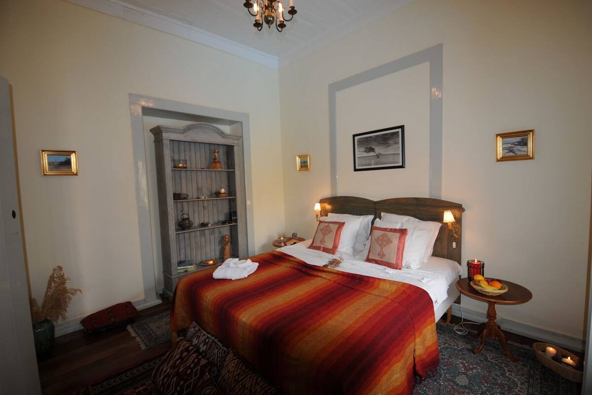 A hotel room with a bed, a nightstand, a small table with fruit, a bookshelf, and a door.