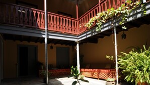 A courtyard with a red balcony, potted plants, and a cobblestone floor. - The Colonial Guest House (São Filipe)