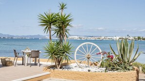 An outdoor seating area with a table and chairs, a large decorative wheel, and plants by the sea. - El Lago Dorado (Formentera)