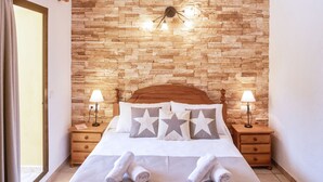 A neatly made bed with star-patterned pillows, two bedside lamps, and a wooden headboard. - El Lago Dorado (Formentera)