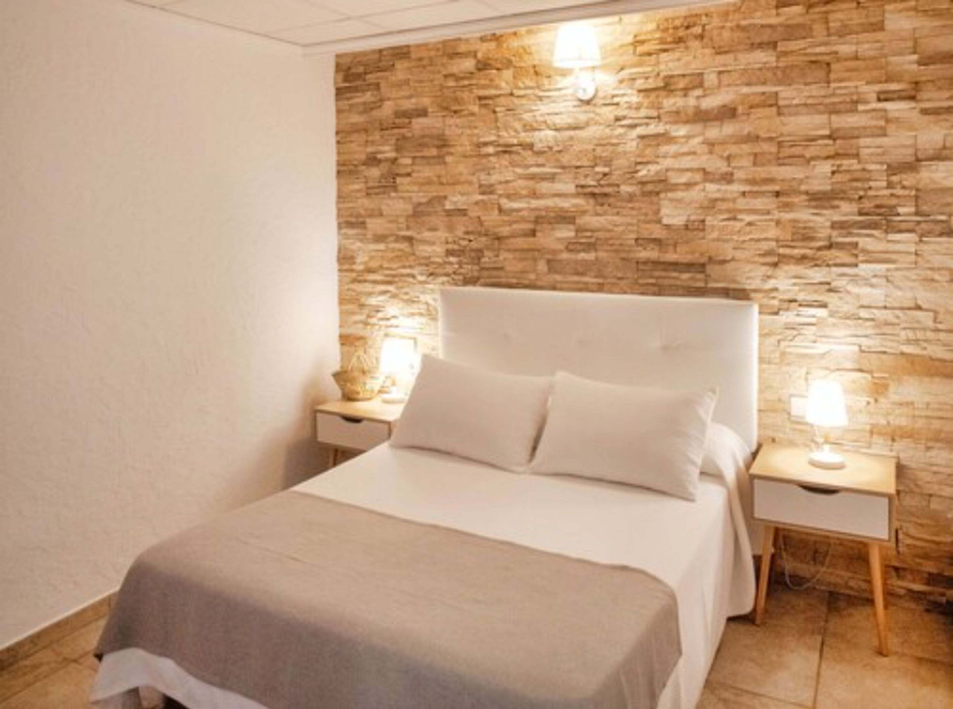 Habitación de hotel con una pared de acento de piedra, una cama con ropa de cama blanca y lámparas de noche.