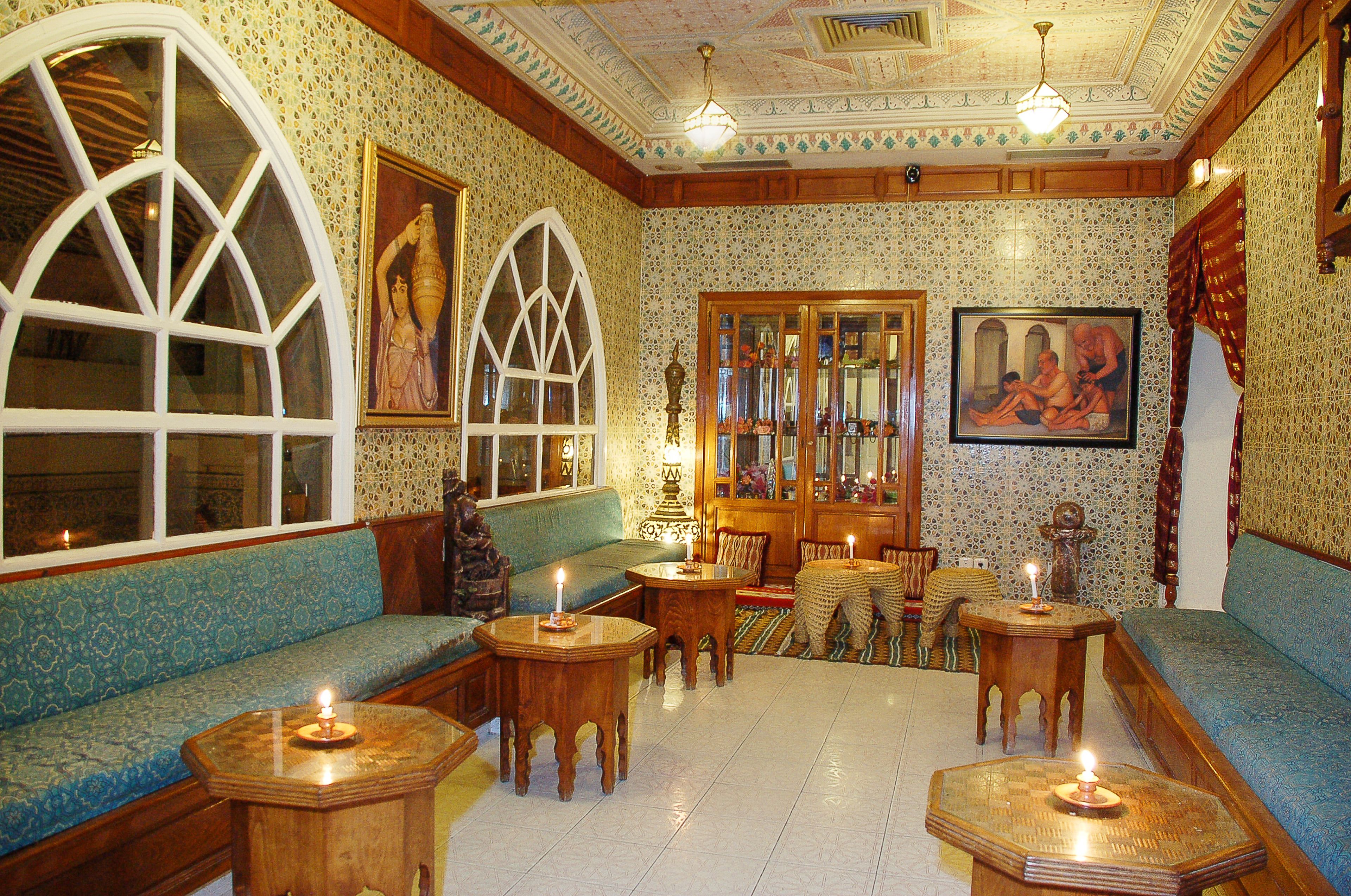A room with a blue patterned sofa, wooden tables, and a large arched window.