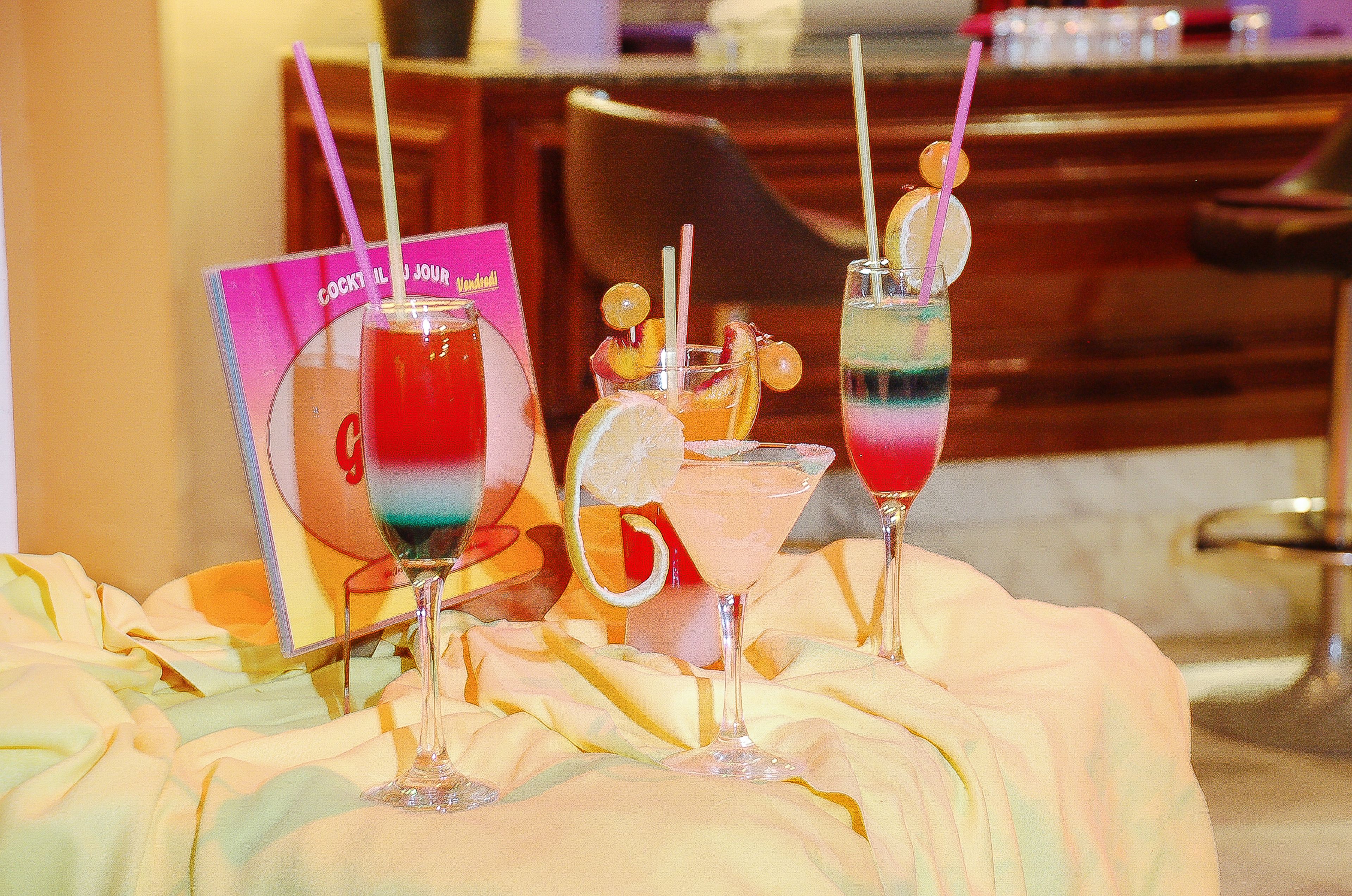 Three cocktails with straws and garnishes on a table with a magazine.