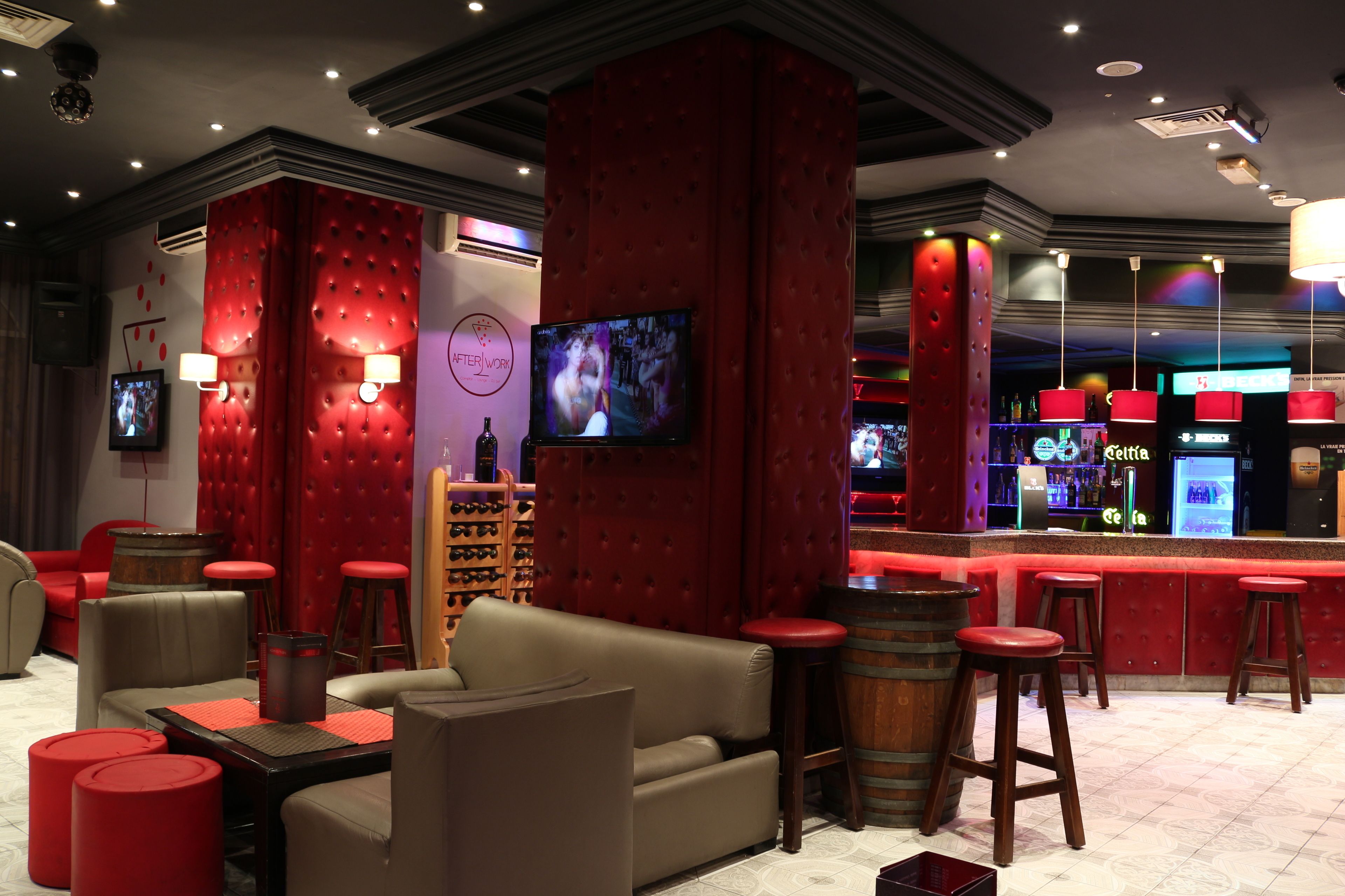 A bar area with red upholstered barstools, a television mounted on the wall, and a bar counter with a minibar.