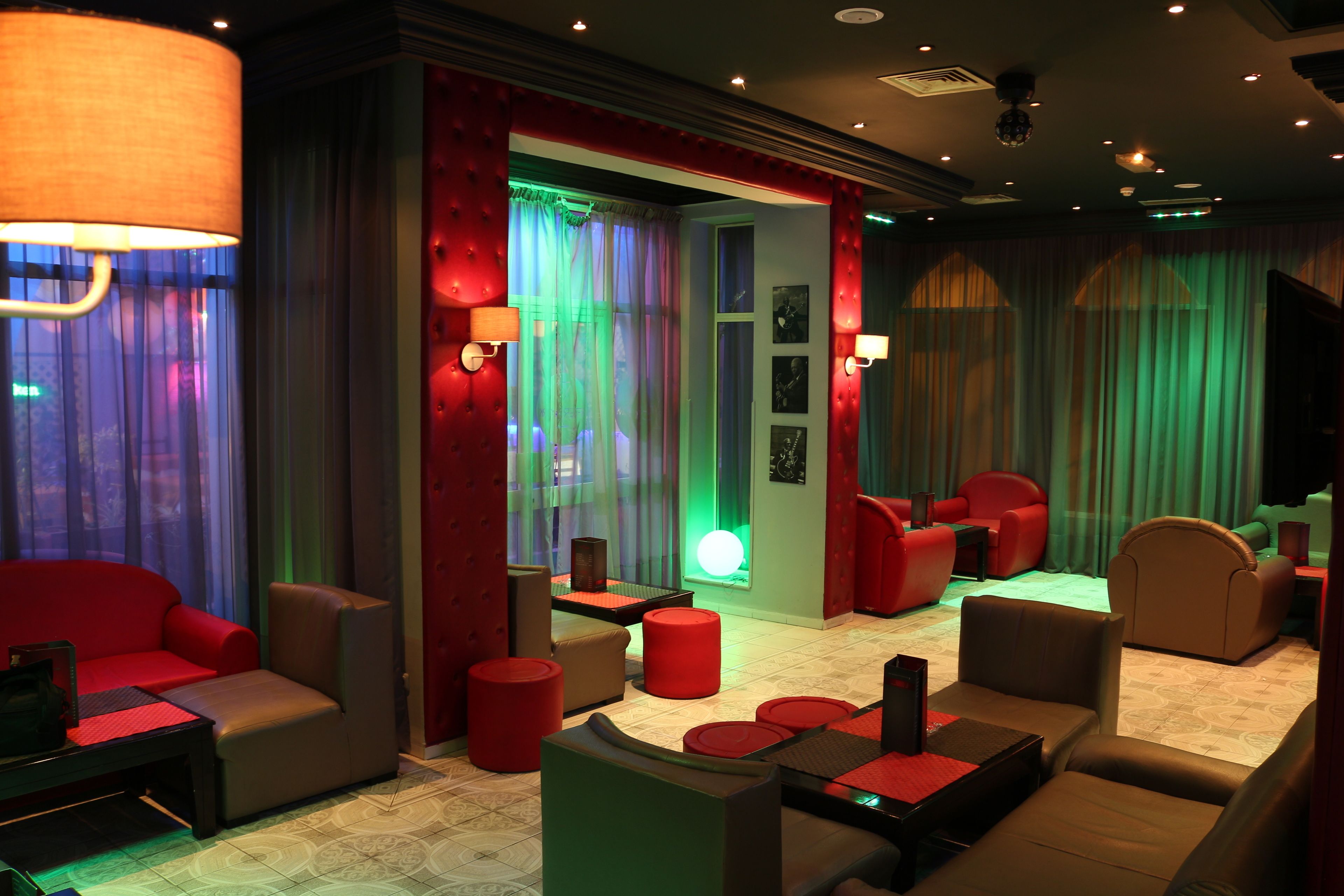 A modern lounge area with red and brown seating, ambient lighting, and a view of the city through large windows.