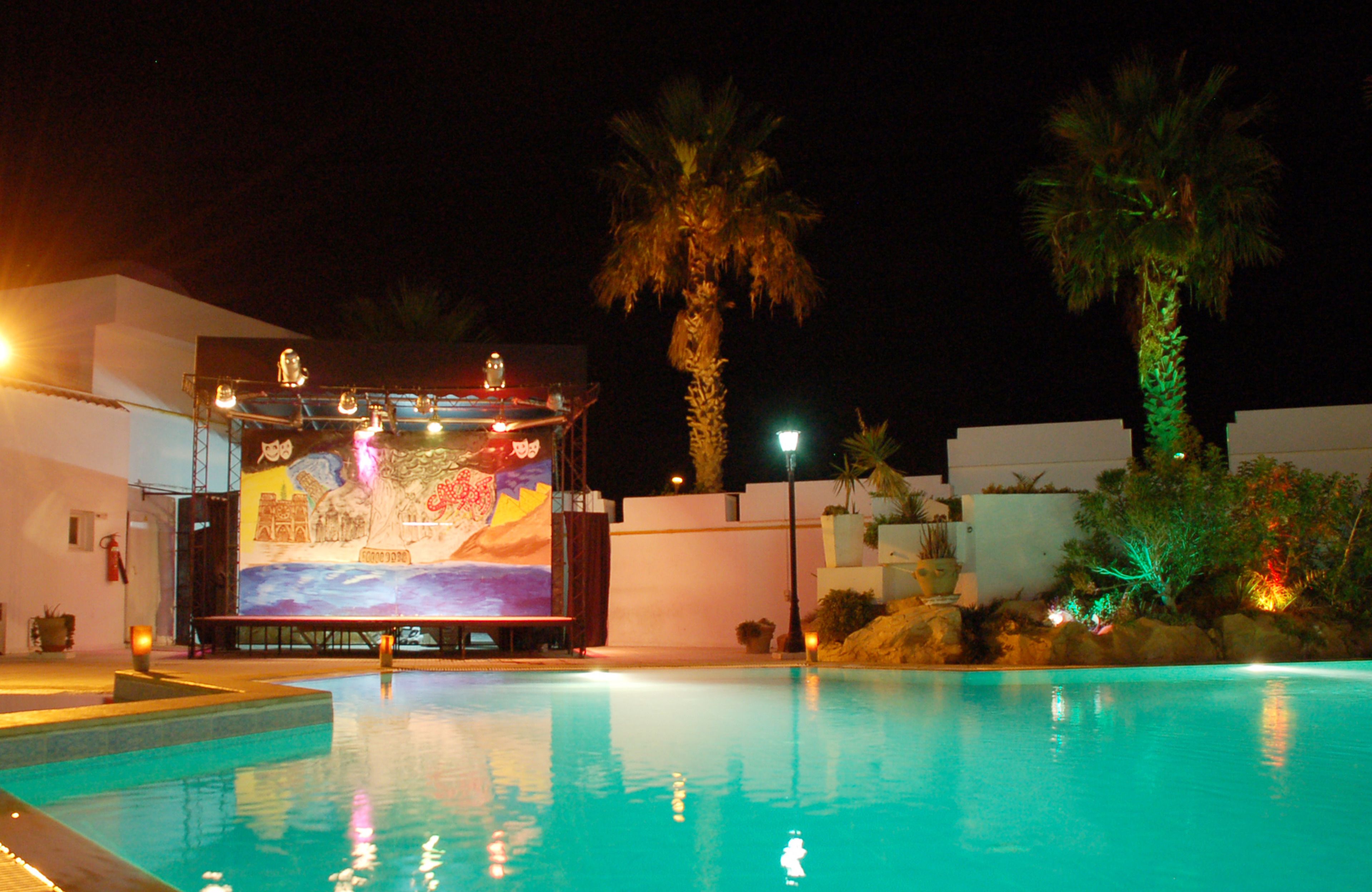 A nighttime pool area with a stage and palm trees.