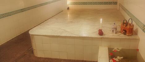 A bathroom with a marble bathtub, a lit candle, and a decorative basket.
