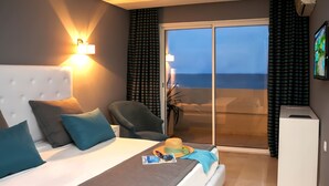 A hotel room with a bed, a chair, a small table, a magazine, and a view of the ocean through a sliding door. - Hotel Byzance (Nabeul)