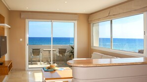 A modern room with a large sliding glass door leading to a balcony with a view of the sea. There is a wooden table and a white cabinet in the room. - Hotel Byzance (Nabeul)