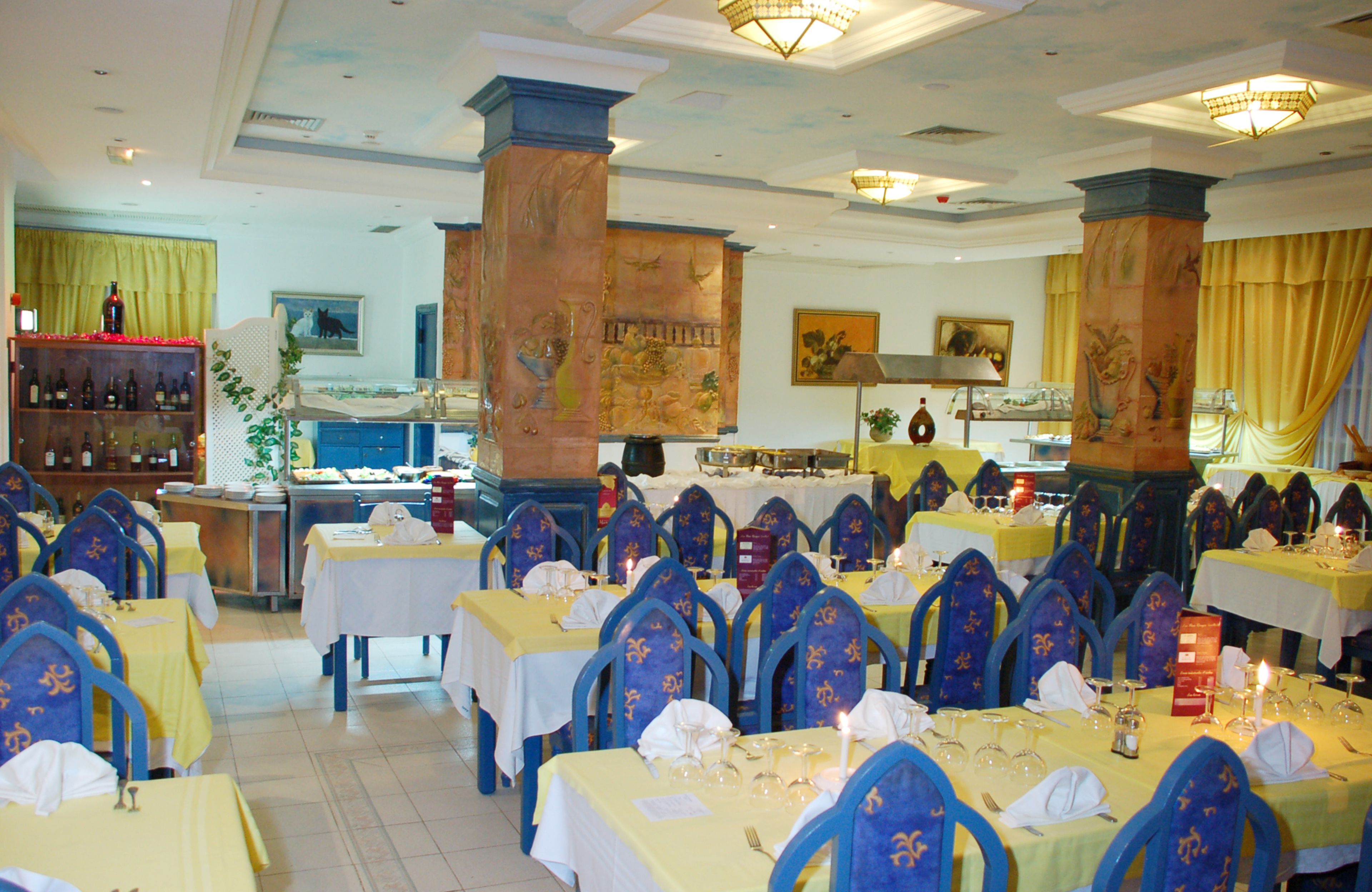 A restaurant with multiple tables and chairs, a bar area, and decorative columns.