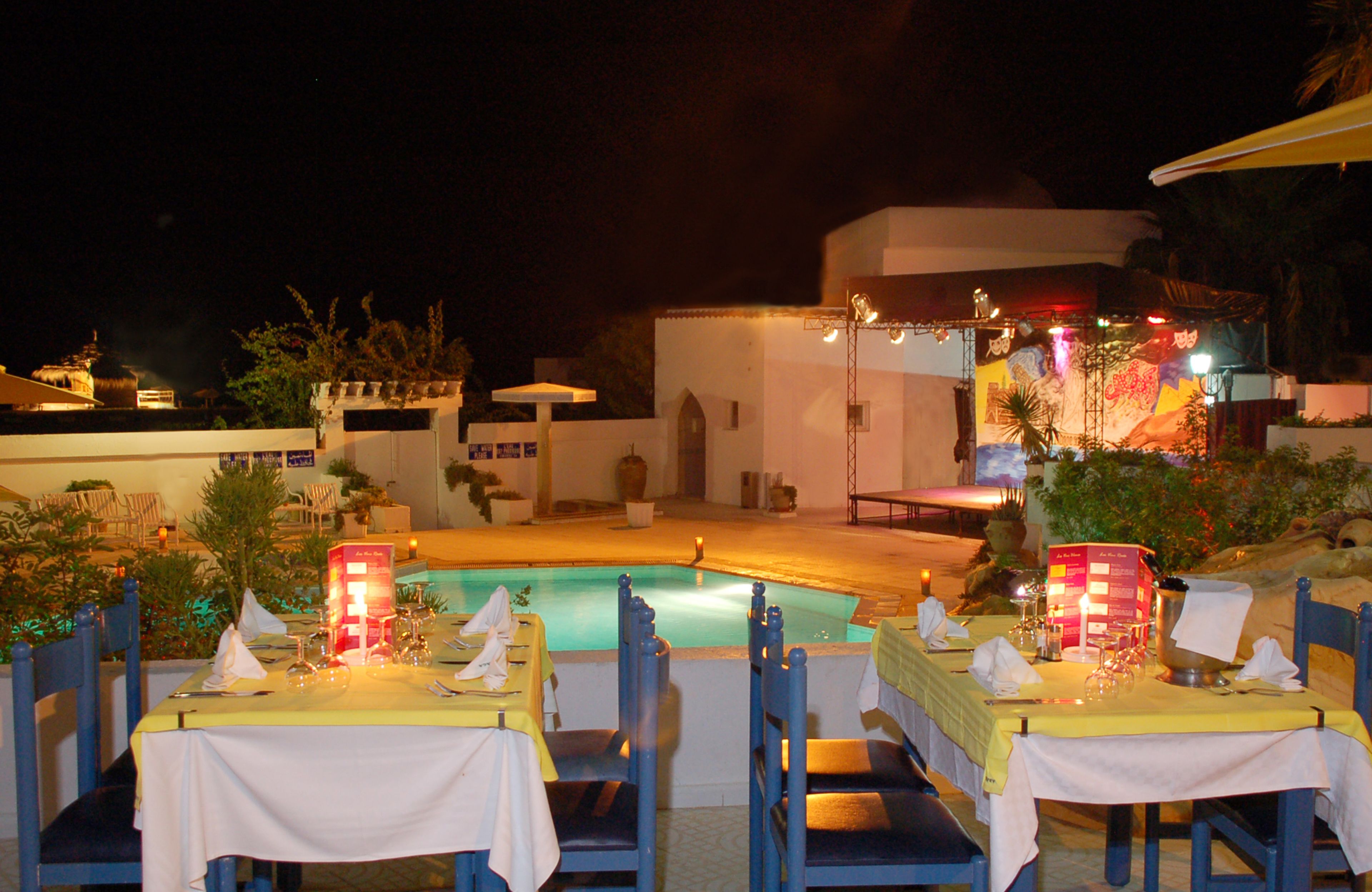 An outdoor dining area with tables and chairs, a pool, and a building with a mural in the background.