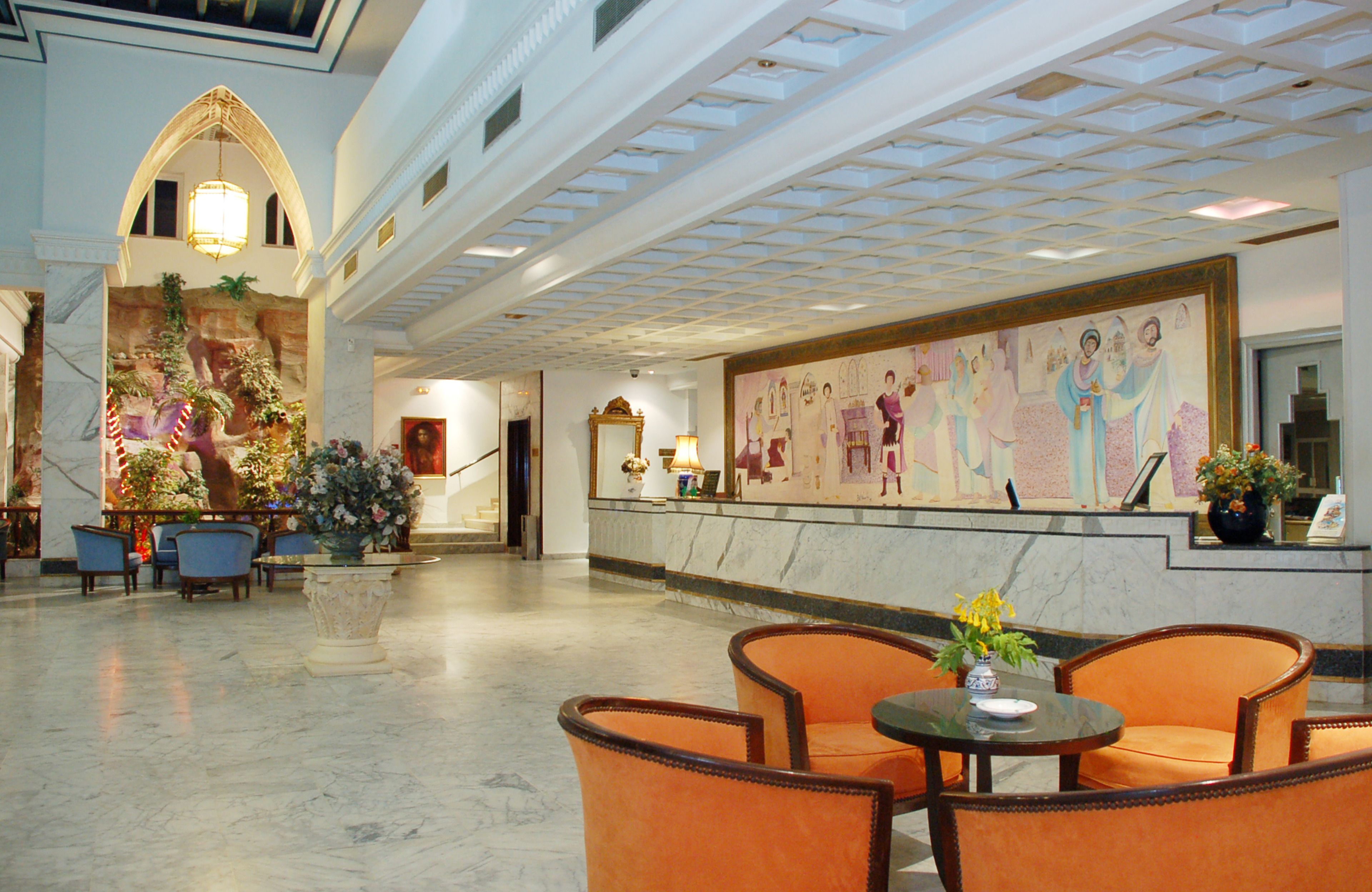 A spacious lobby with marble flooring, a large mural, and seating areas with orange chairs.