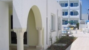 A white building with a covered outdoor seating area and a clear sky. - Hotel Les Citronniers (Hammamet)