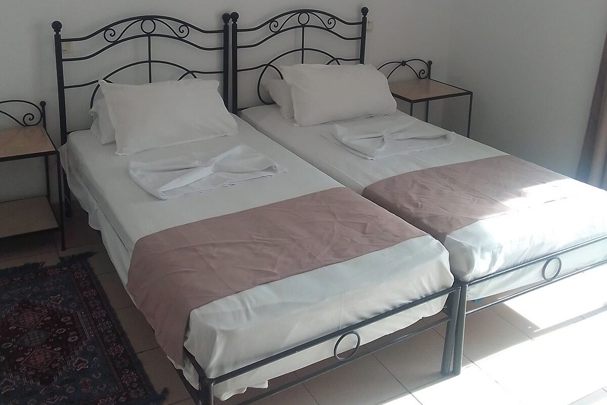 A room with two beds, a nightstand, a lamp, and an air conditioning unit.