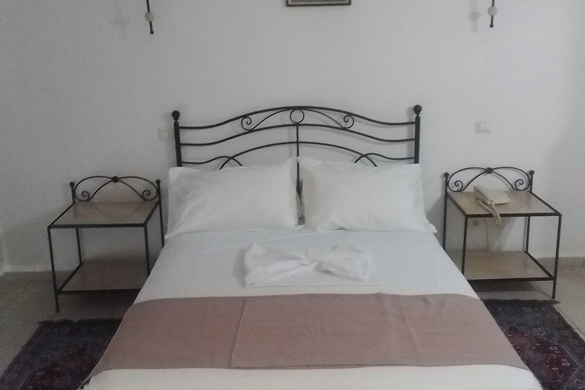 A single bed with a metal frame, two bedside tables, a wall-mounted picture, and a wall-mounted lamp.