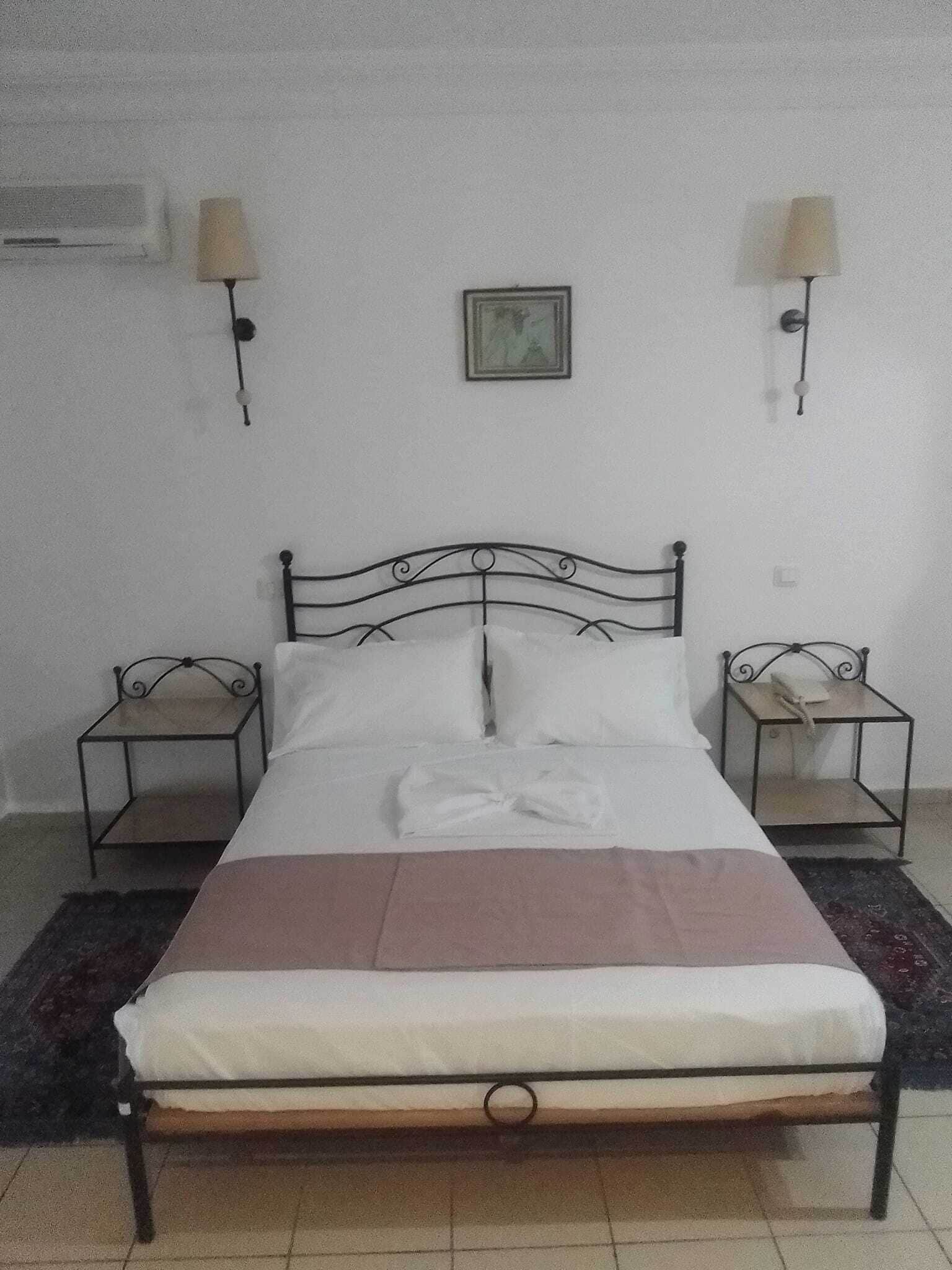A single bed with a metal frame, two bedside tables, a wall-mounted picture, and a wall-mounted lamp.