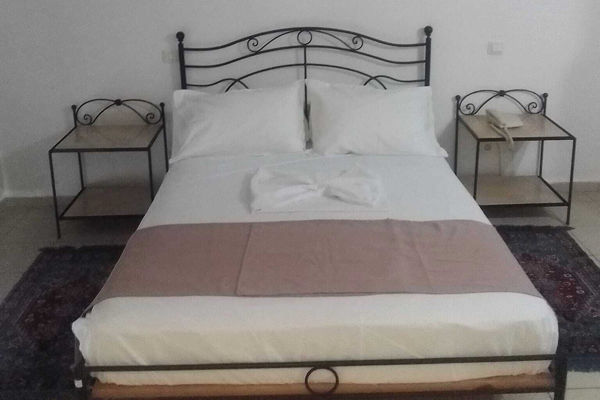 A single bed with a metal frame, two bedside tables, a wall-mounted picture, and a wall-mounted lamp.