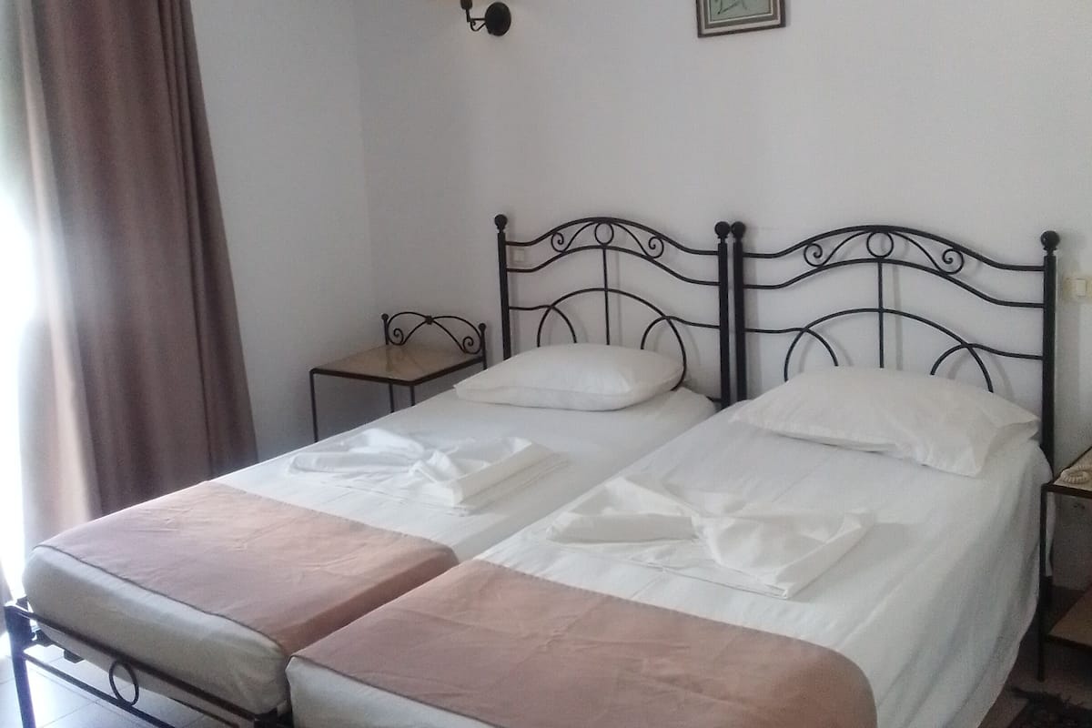 A double bed with a headboard, a bedside table, a wall-mounted air conditioner, a wall-mounted lamp, and a window with curtains.