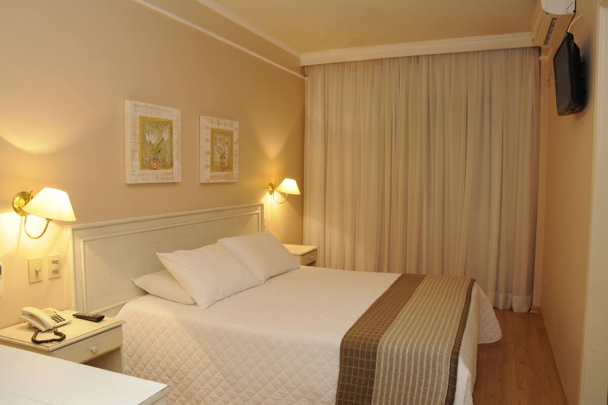 A hotel room with a bed, bedside lamps, a telephone, and a television mounted on the wall.