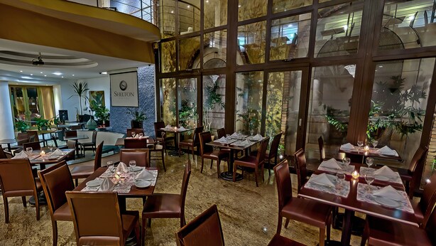A restaurant with multiple dining tables, chairs, and a large window offering a view of the interior. - Shelton Hotel (Serra Negra)