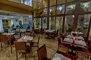 A restaurant with multiple dining tables, chairs, and a large window offering a view of the interior. - Shelton Hotel (Serra Negra)