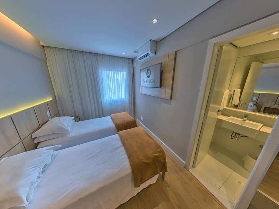 A hotel room with two beds, a bathroom with a glass shower, and a sign on the wall.