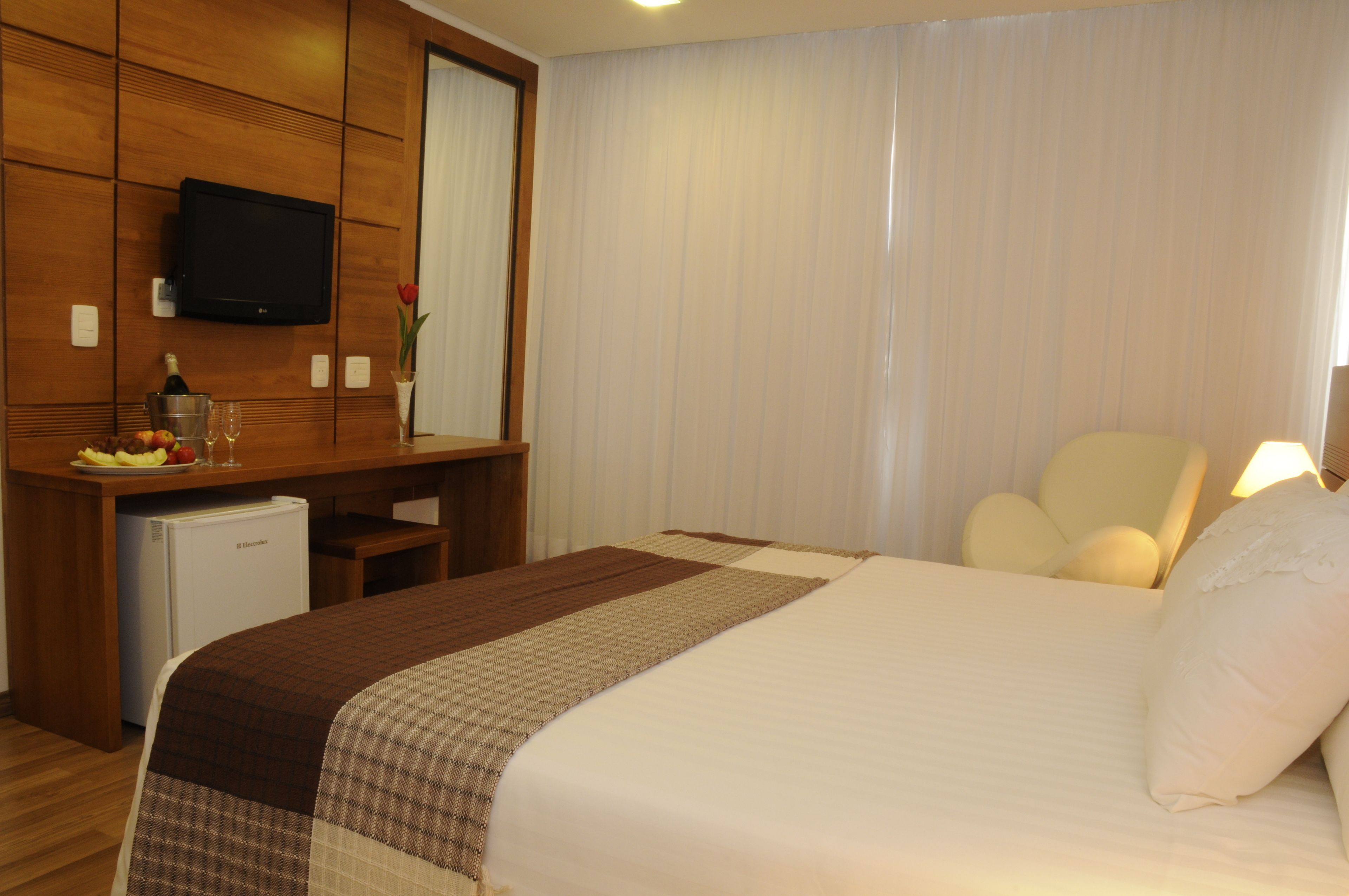 Ein Hotelzimmer mit Bett, Schreibtisch, Fernseher, Minibar und Stuhl.