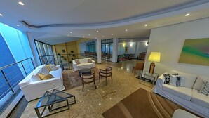 A spacious living area with a white sofa, a glass coffee table, and a dining area in the background. - Shelton Hotel (Serra Negra)