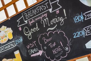 A chalkboard with breakfast options and prices, including Continental for $25, and a sign pointing to a tour. - Hacienda Fisherman's Village Koh Samui (Koh Samui)