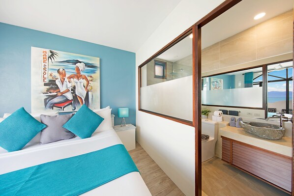 A hotel room with a bed, a nightstand, a bathroom with a large mirror, and a view of the sea. - Hacienda Fisherman's Village Koh Samui (Koh Samui)