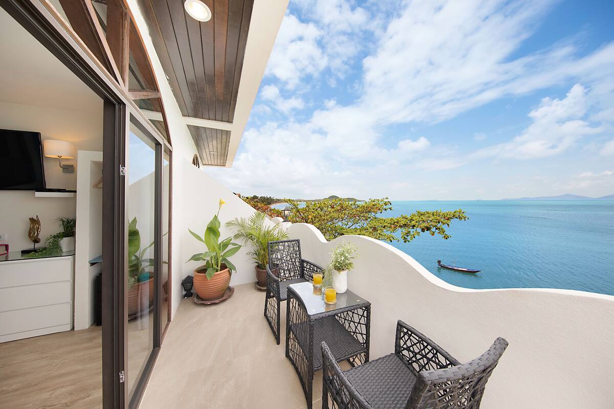A balcony with a view of the sea, a table with chairs, and potted plants.